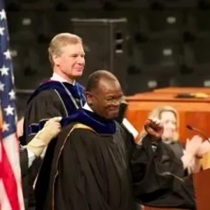 A man in graduation robes standing next to another man.