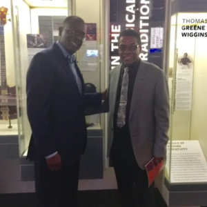 Two men in suits and ties standing next to a glass case.