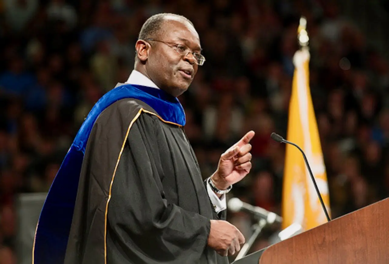 A man in graduation robes speaking at a podium.
