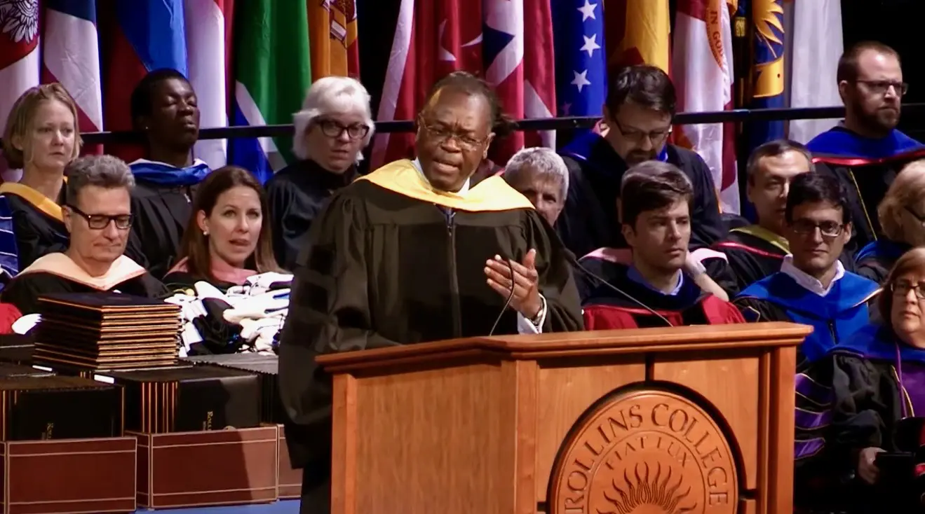 A man in graduation gown speaking at podium.