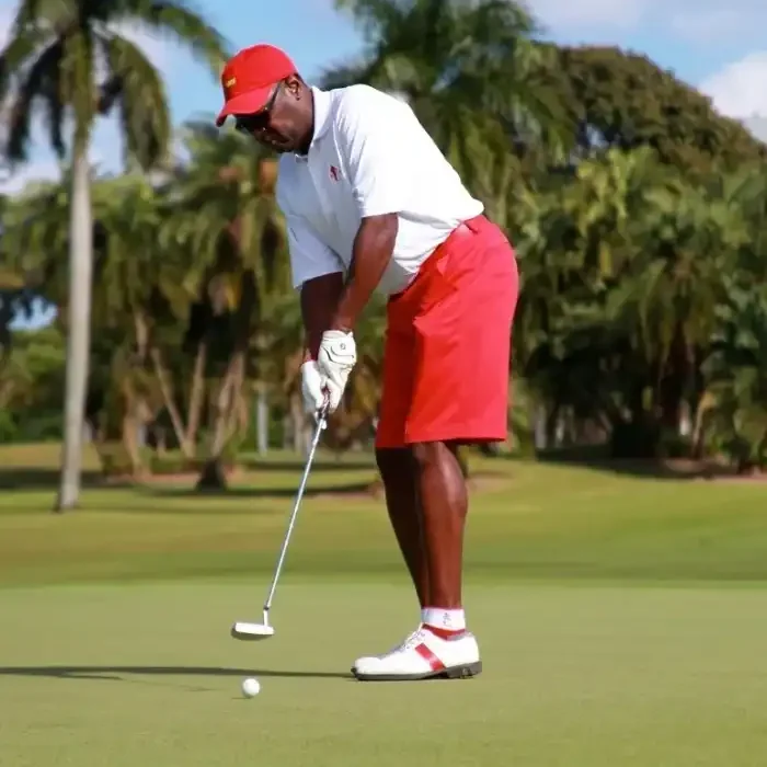 A man in red shorts and white shirt playing golf.